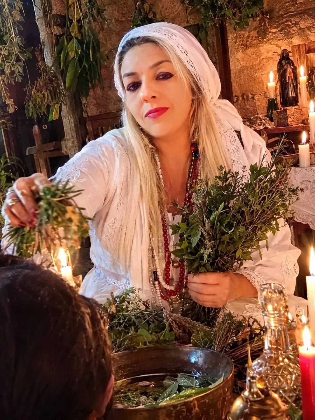 Paloma de lenço de renda branca e colares vermelhos, segurando um maço de ervas frescas sobre uma bacia de água com folhas